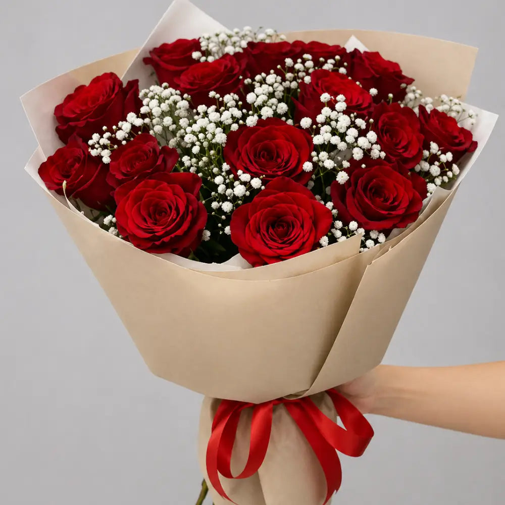Bouquet of red roses with a red ribbon held by a hand on a gray background