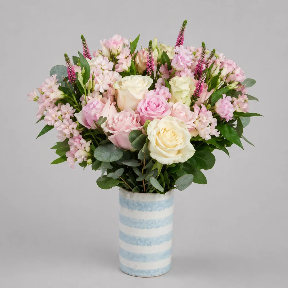 Bouquet of pink and white flowers in a striped vase on a gray background