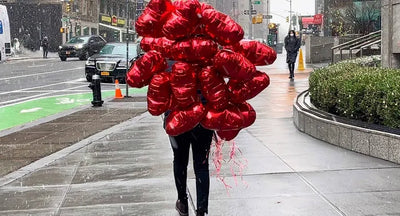Person carrying a large number of red balloons on a city street