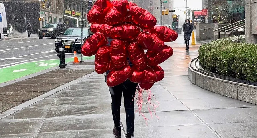 Person carrying a large number of red balloons on a city street
