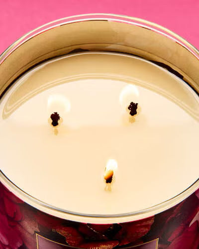 Close-up of a candle with three wicks inside a decorative container.