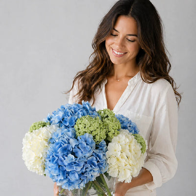 Woman holding a bouquet of blue, white, and green flowers against a gray background